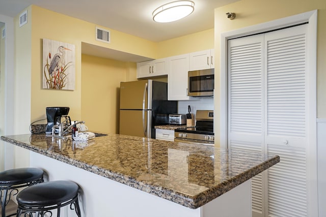 kitchen with dark stone countertops, stainless steel appliances, kitchen peninsula, and white cabinets