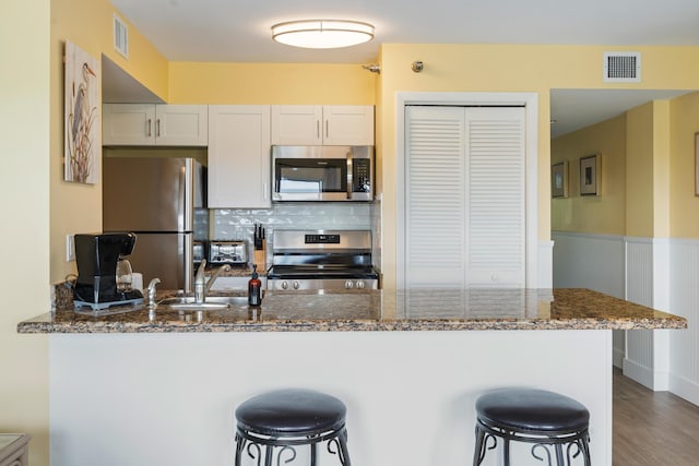 kitchen with a breakfast bar area, white cabinetry, appliances with stainless steel finishes, kitchen peninsula, and dark stone counters