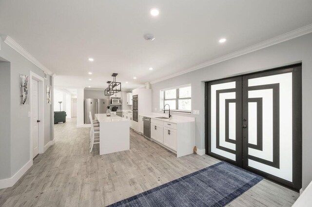 kitchen featuring pendant lighting, white cabinets, ornamental molding, a center island, and stainless steel appliances