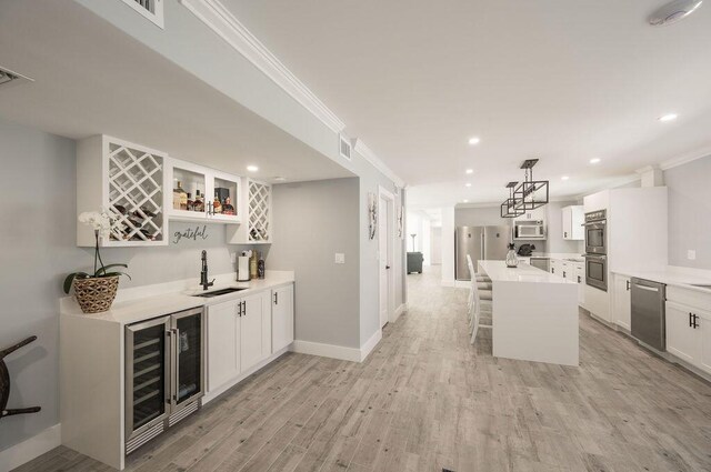 kitchen featuring a breakfast bar, white cabinetry, hanging light fixtures, stainless steel appliances, and a center island with sink