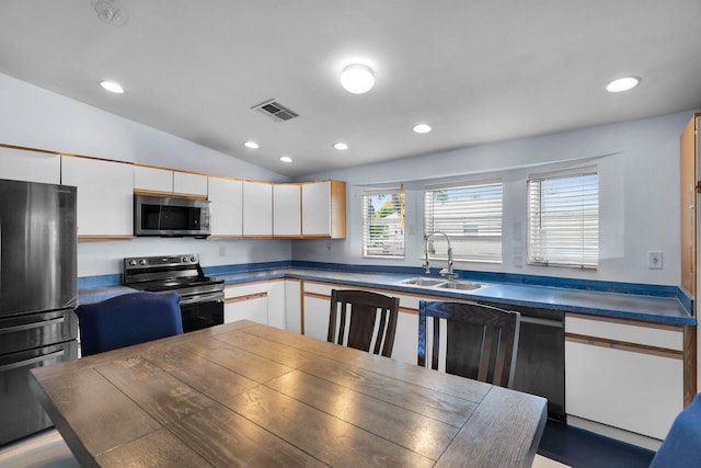 kitchen featuring lofted ceiling, dark countertops, appliances with stainless steel finishes, and a sink