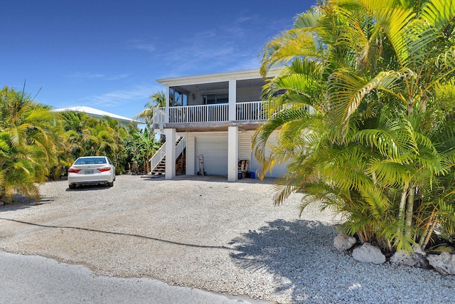 coastal inspired home with a porch, stairs, a garage, and driveway