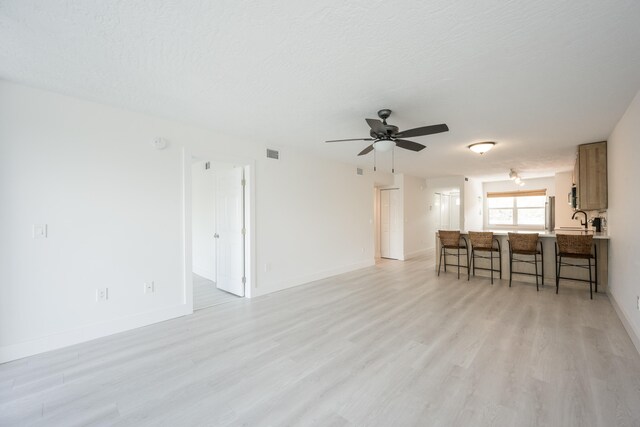 living room with sink, light hardwood / wood-style flooring, a textured ceiling, and ceiling fan