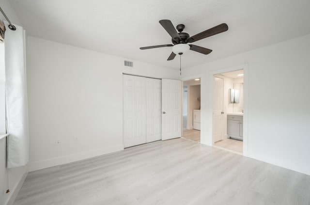 unfurnished bedroom featuring washer / dryer, light wood-type flooring, ceiling fan, ensuite bath, and a closet