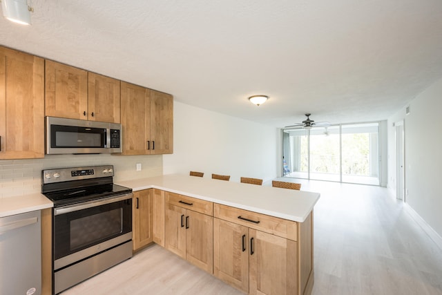 kitchen featuring tasteful backsplash, light hardwood / wood-style flooring, kitchen peninsula, and appliances with stainless steel finishes