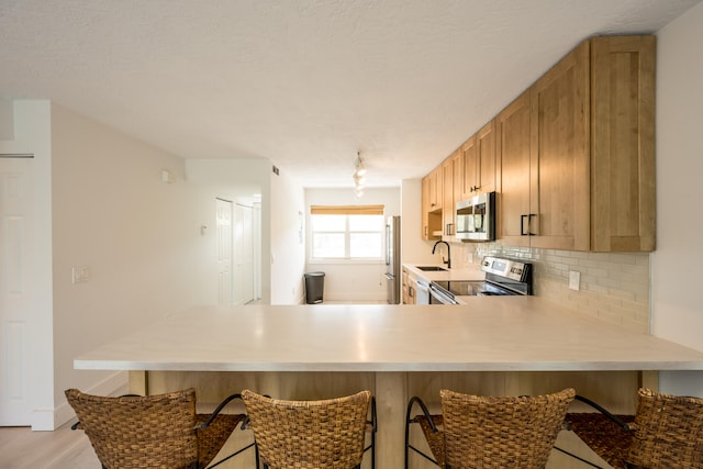 kitchen with light brown cabinetry, sink, decorative backsplash, kitchen peninsula, and stainless steel appliances