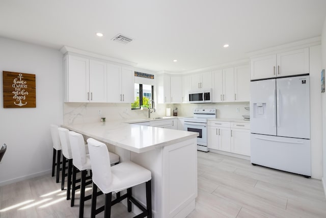 kitchen featuring white cabinetry, white appliances, a kitchen breakfast bar, and kitchen peninsula