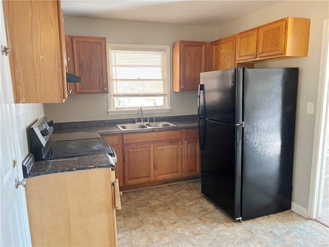 kitchen featuring brown cabinetry, dark countertops, freestanding refrigerator, under cabinet range hood, and a sink