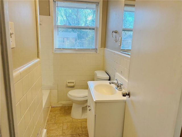 bathroom with toilet, a wainscoted wall, tile walls, and vanity