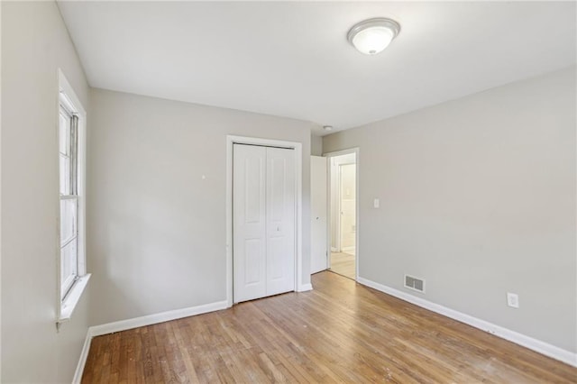 unfurnished bedroom with visible vents, a closet, baseboards, and wood finished floors