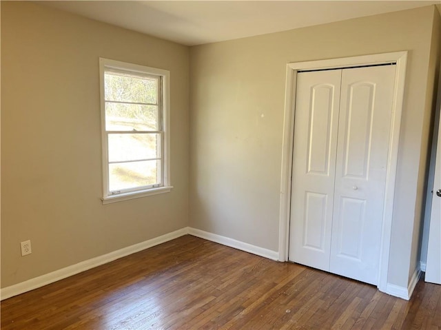 unfurnished bedroom featuring dark wood-style floors, baseboards, and a closet