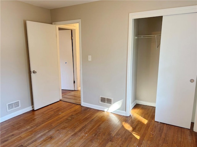 unfurnished bedroom with wood-type flooring, visible vents, and a closet