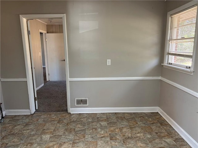 empty room with stone finish flooring, visible vents, and baseboards