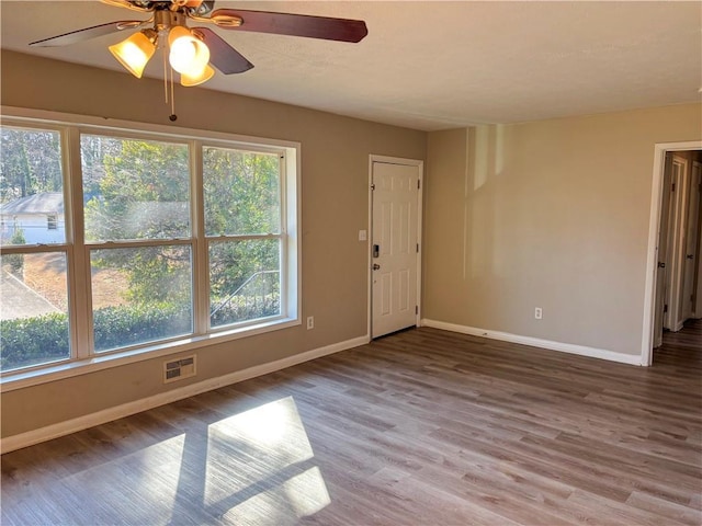 empty room featuring a ceiling fan, visible vents, baseboards, and wood finished floors