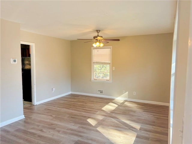 spare room with light wood-style floors, a ceiling fan, visible vents, and baseboards