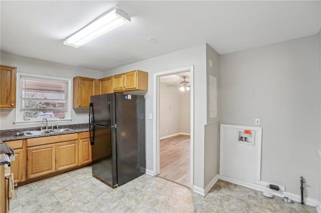 kitchen featuring ceiling fan, a sink, baseboards, freestanding refrigerator, and dark countertops