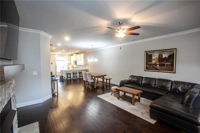 living room with ceiling fan, a stone fireplace, crown molding, and dark wood-type flooring