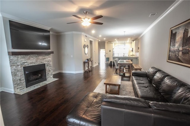 living room featuring ceiling fan, dark hardwood / wood-style flooring, crown molding, and a stone fireplace