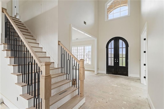 entrance foyer with stairway, a healthy amount of sunlight, a towering ceiling, and french doors