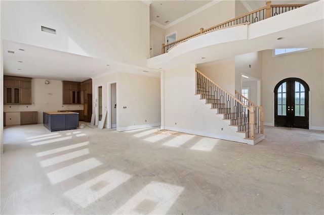unfurnished living room with stairs, crown molding, french doors, and a towering ceiling