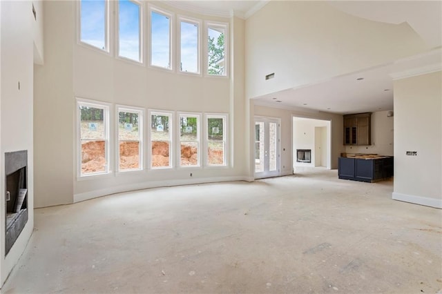 unfurnished living room with a fireplace, crown molding, plenty of natural light, and a towering ceiling