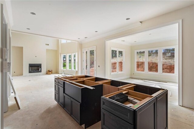 kitchen featuring dark cabinets, a kitchen island, crown molding, a fireplace, and open floor plan