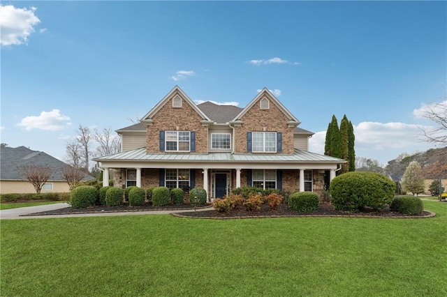view of front of home with brick siding, a porch, a front yard, a standing seam roof, and metal roof