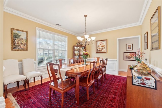 dining space with crown molding, a chandelier, dark wood finished floors, a wainscoted wall, and visible vents