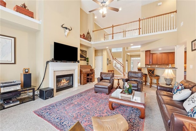 living room featuring carpet floors, a towering ceiling, stairway, and ceiling fan