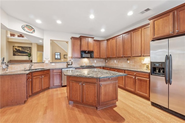 kitchen featuring visible vents, appliances with stainless steel finishes, a sink, stone countertops, and light wood finished floors