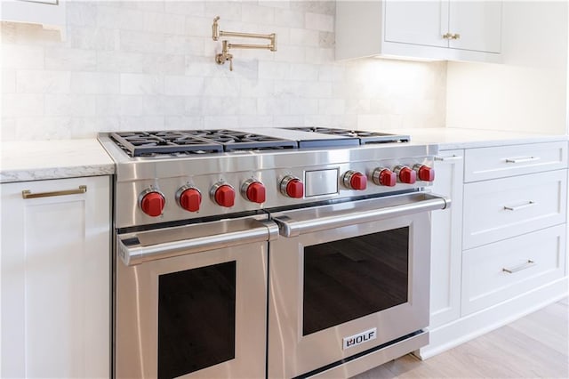 kitchen with white cabinetry, light stone counters, tasteful backsplash, and premium stove