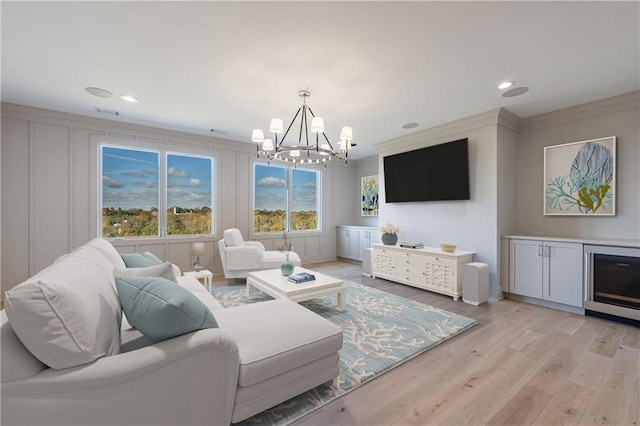 living room featuring ornamental molding, beverage cooler, light hardwood / wood-style flooring, and a notable chandelier