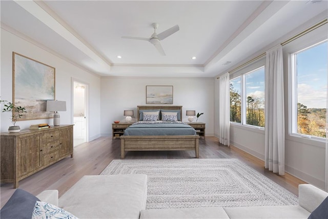 bedroom featuring ceiling fan, ensuite bathroom, a raised ceiling, and light hardwood / wood-style flooring