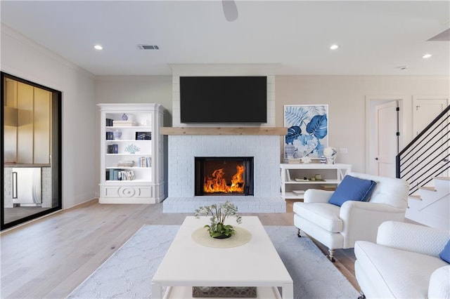 living room featuring crown molding, a brick fireplace, and light hardwood / wood-style flooring