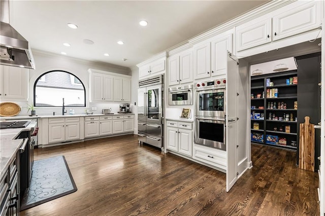 15595 Birmingham Hwy, Alpharetta, GA 30004 - kitchen with appliances with stainless steel finishes, wall chimney exhaust hood, white cabinetry, dark wood finished floors, and ornamental molding