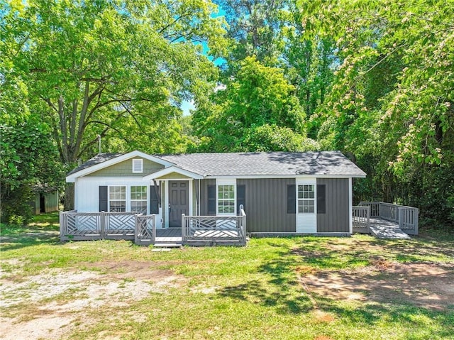 view of front facade featuring roof with shingles, a front lawn, and a wooden deck