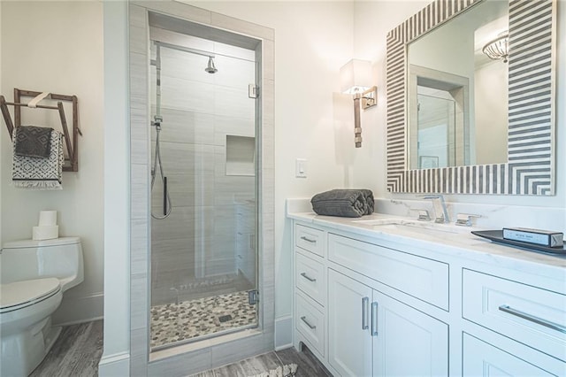 bathroom with a shower stall, toilet, vanity, and wood finished floors