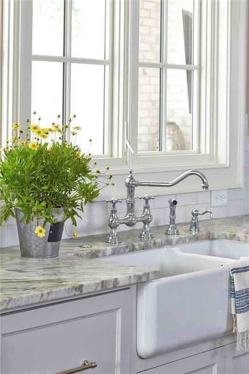 kitchen view of white cabinets, light stone countertops, backsplash, and a sink