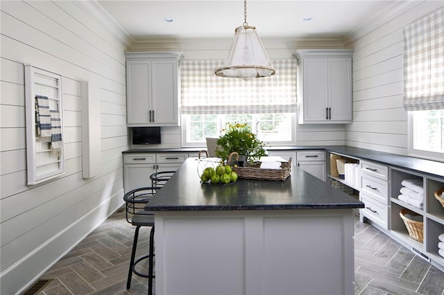 kitchen with wooden walls, ornamental molding, dark countertops, a kitchen island, and a breakfast bar