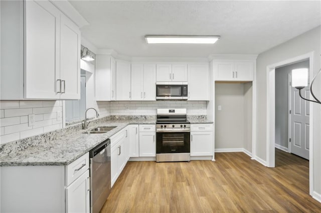 kitchen featuring appliances with stainless steel finishes, sink, white cabinets, light stone countertops, and light wood-type flooring