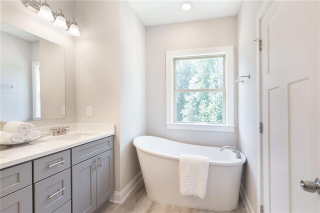 full bath with a freestanding bath, wood finished floors, vanity, and baseboards