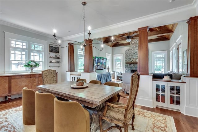 dining room featuring hardwood / wood-style flooring, decorative columns, a stone fireplace, ornamental molding, and ceiling fan