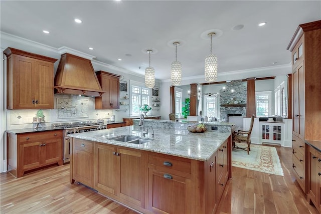 kitchen featuring pendant lighting, custom exhaust hood, light wood-type flooring, sink, and a fireplace