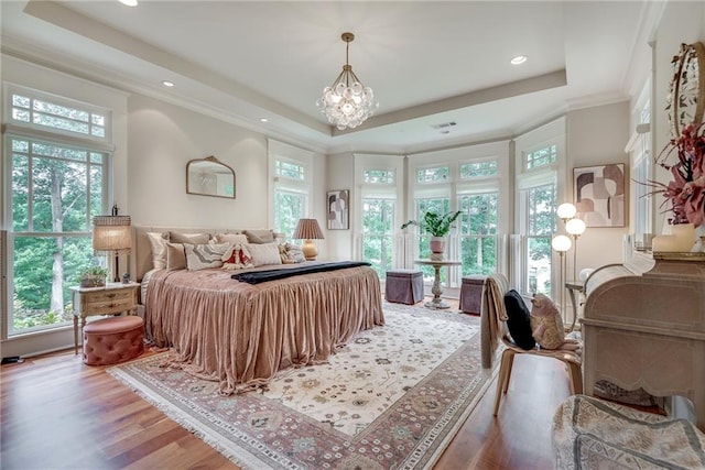 bedroom with multiple windows, a tray ceiling, an inviting chandelier, and hardwood / wood-style flooring