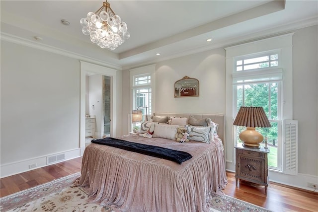 bedroom with a chandelier, light hardwood / wood-style floors, a raised ceiling, and ensuite bathroom