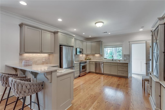 kitchen featuring ornamental molding, kitchen peninsula, appliances with stainless steel finishes, light wood-type flooring, and a kitchen bar