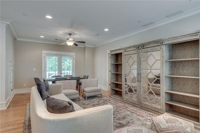 living room with ceiling fan, ornamental molding, french doors, a barn door, and hardwood / wood-style floors