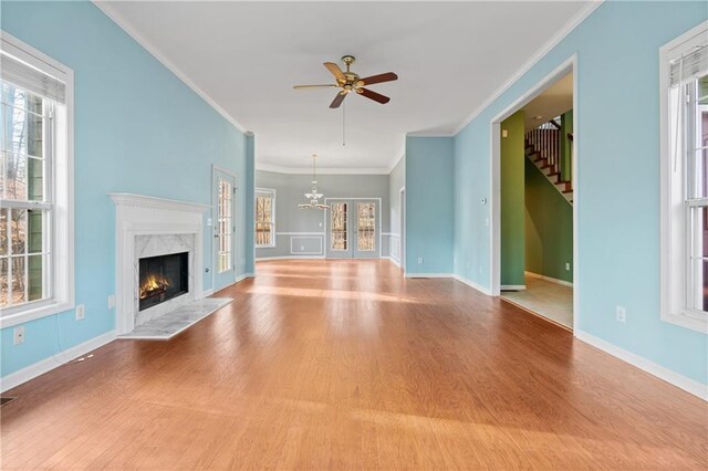 unfurnished living room with a premium fireplace, wood-type flooring, ceiling fan with notable chandelier, and ornamental molding