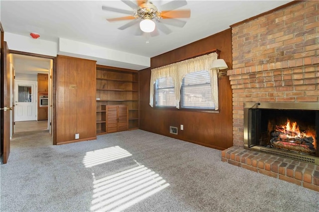 unfurnished living room featuring a brick fireplace, light colored carpet, wood walls, and ceiling fan