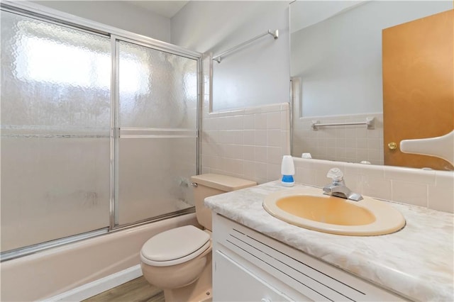 full bathroom with wood-type flooring, vanity, tile walls, toilet, and combined bath / shower with glass door